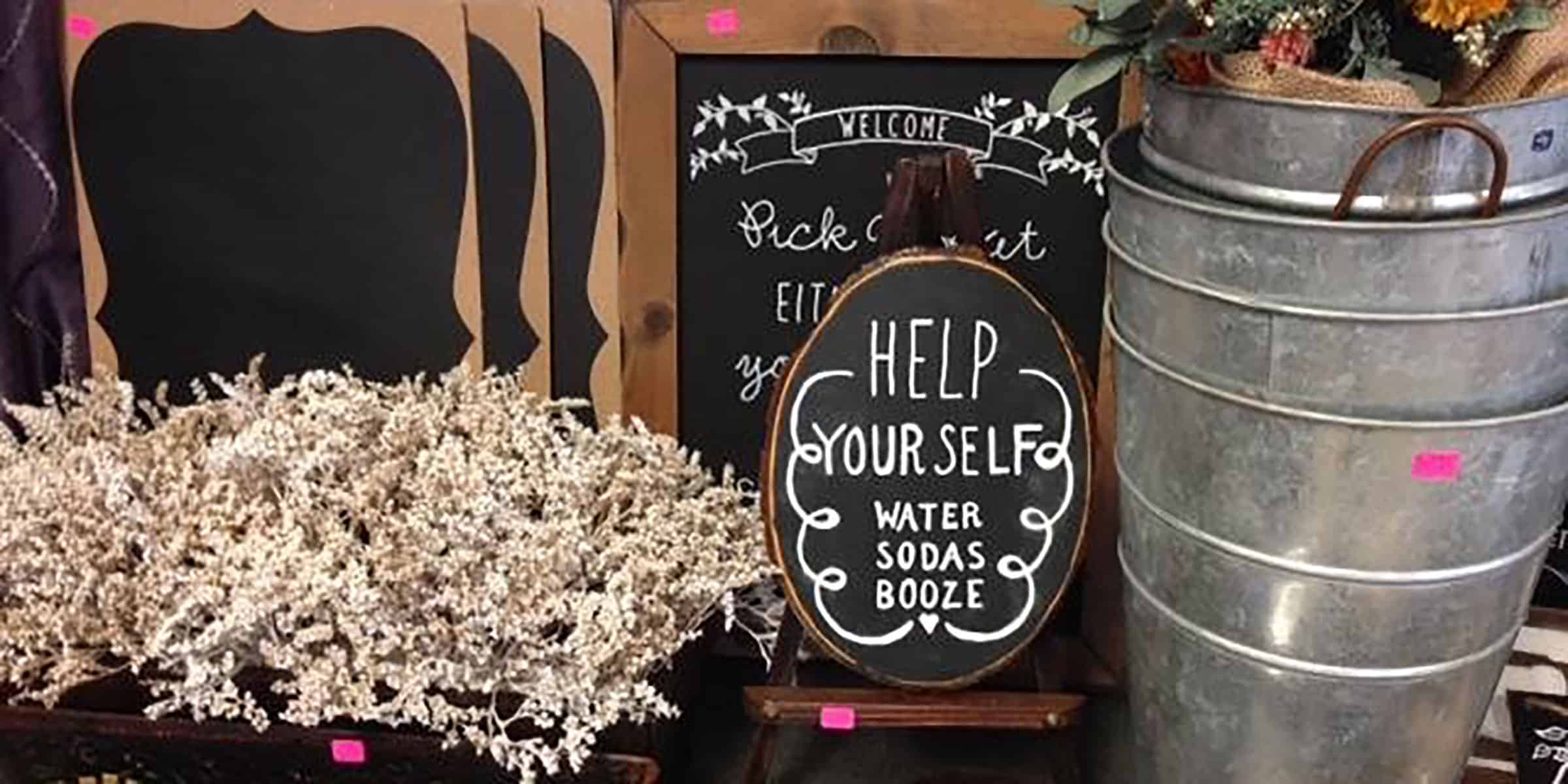 Assorted decorative signs, a bucket with dried flowers, and a metal tub with a chalkboard sign reading "Help Yourself: Water, Sodas, Booze".