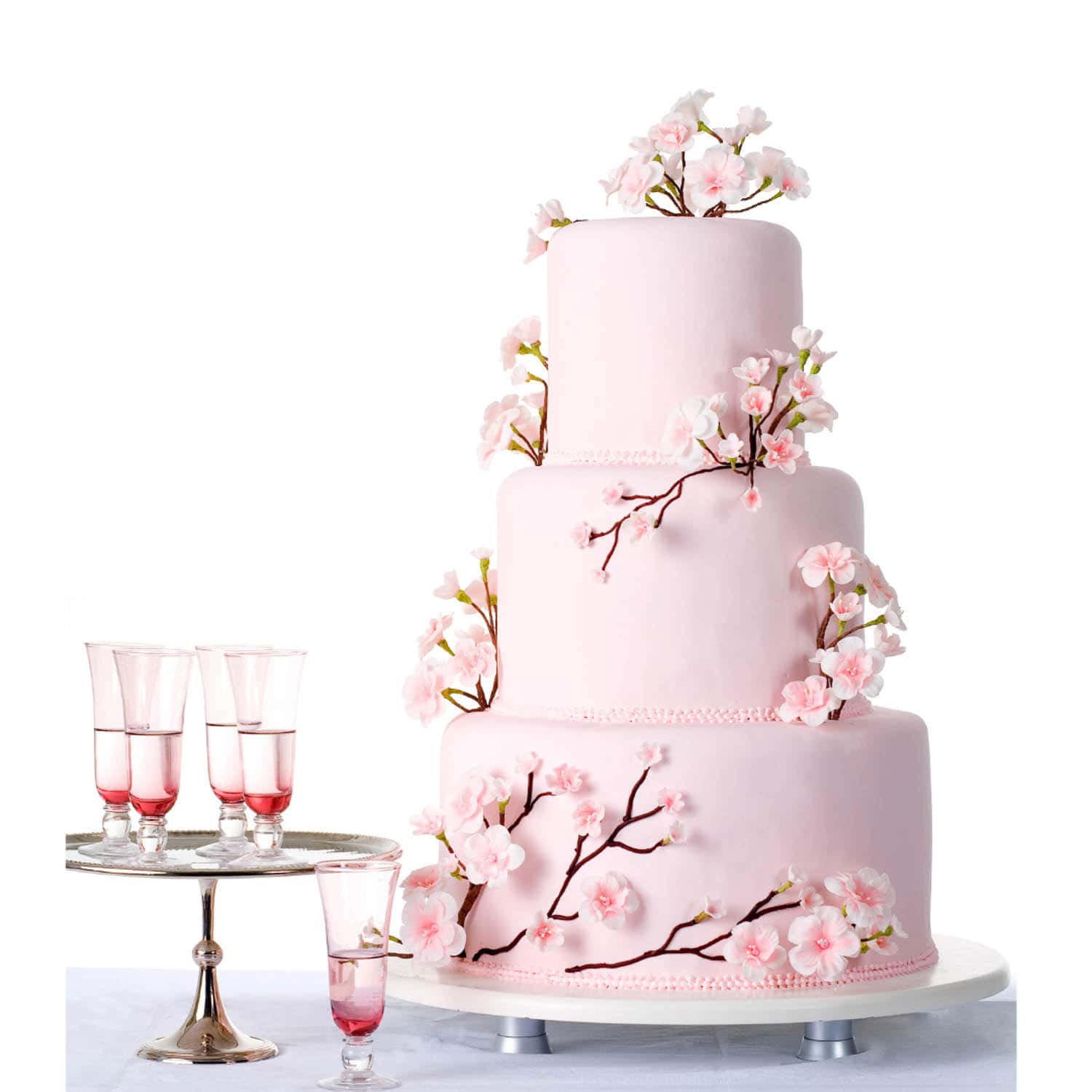 Three-tiered pink cake decorated with cherry blossom flowers, accompanied by four glasses of pink beverage on a silver tray.