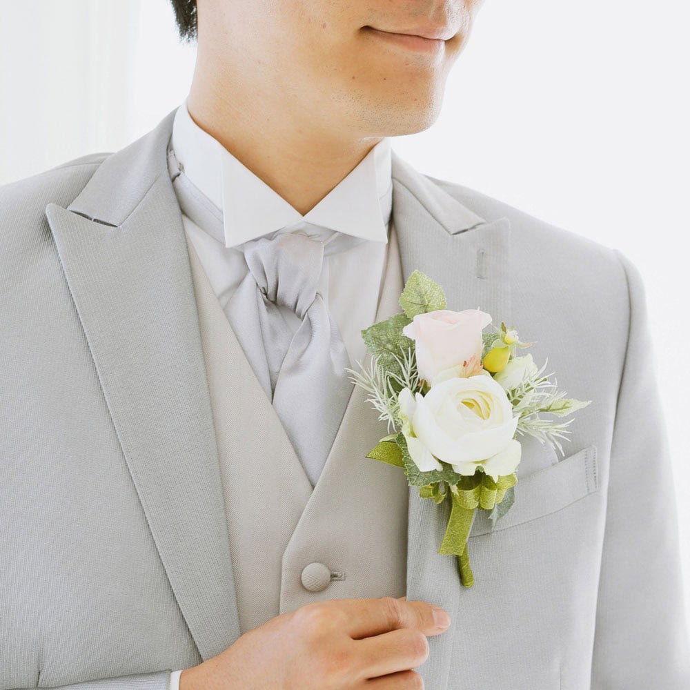 A man in a light gray suit adjusts his jacket, showing a boutonniere with white and pink roses pinned to his lapel.