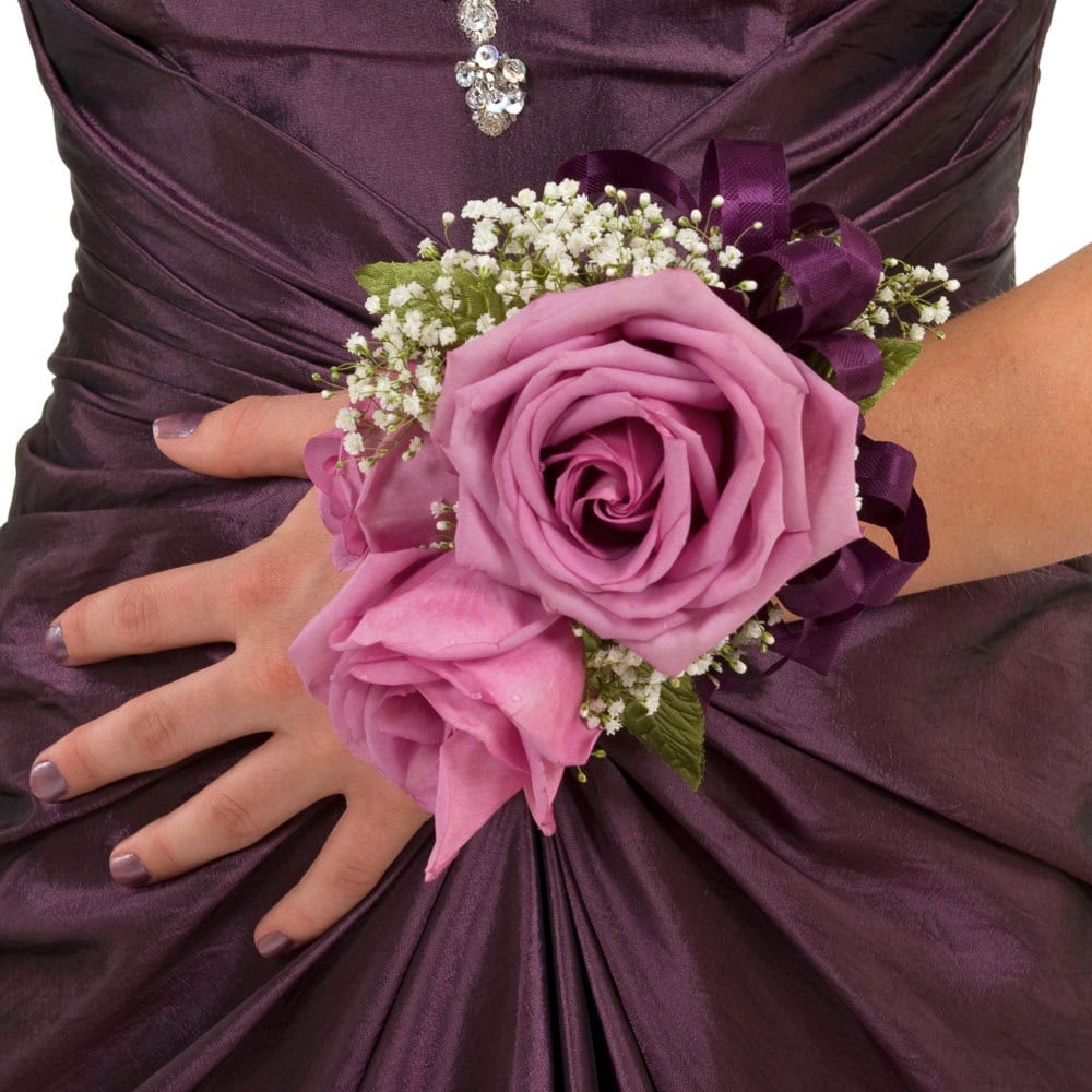 A woman in a purple dress wears a wrist corsage made of pink roses, baby's breath, and purple ribbon.