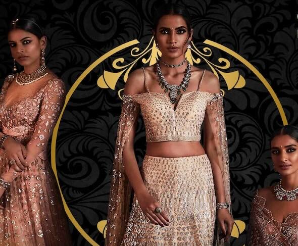 Three women pose in ornate, embellished lehengas and jewelry against a dark, decorative background with gold accents.