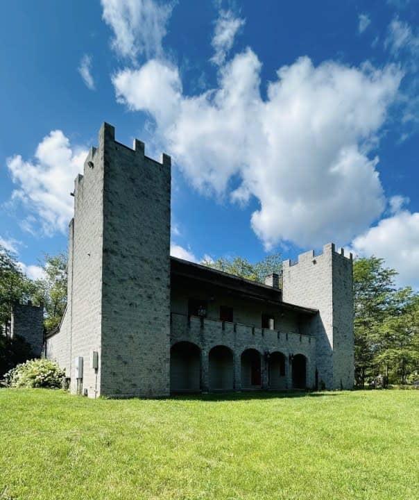 A stone building with two castle-like towers and arched doorways stands on a grassy lawn under a partly cloudy sky.